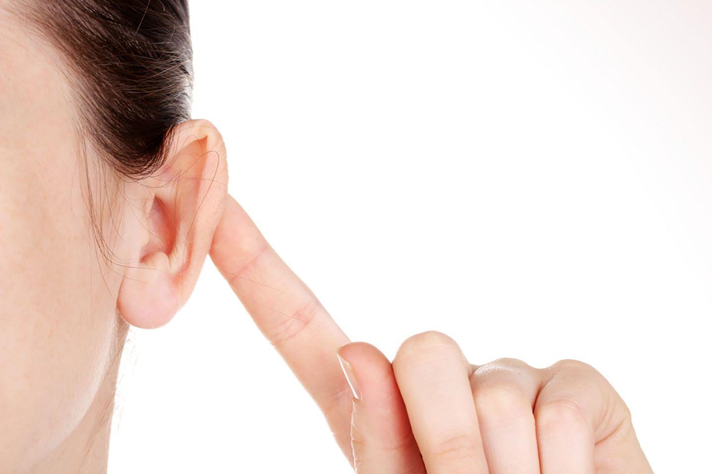 A woman pushes her ear forward with her finger